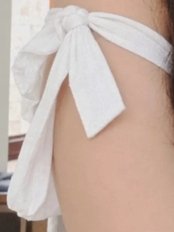 Detail of a white ribbon tied on Manu’s shoulder.